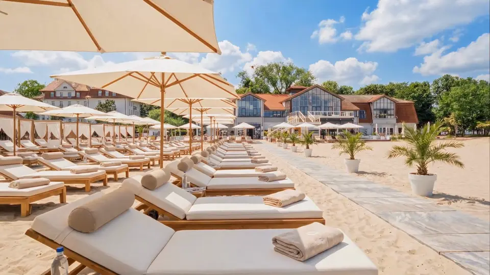 Leżaki z materacami pod parasolami na plaży MUDO, w tle budynki przy plaży