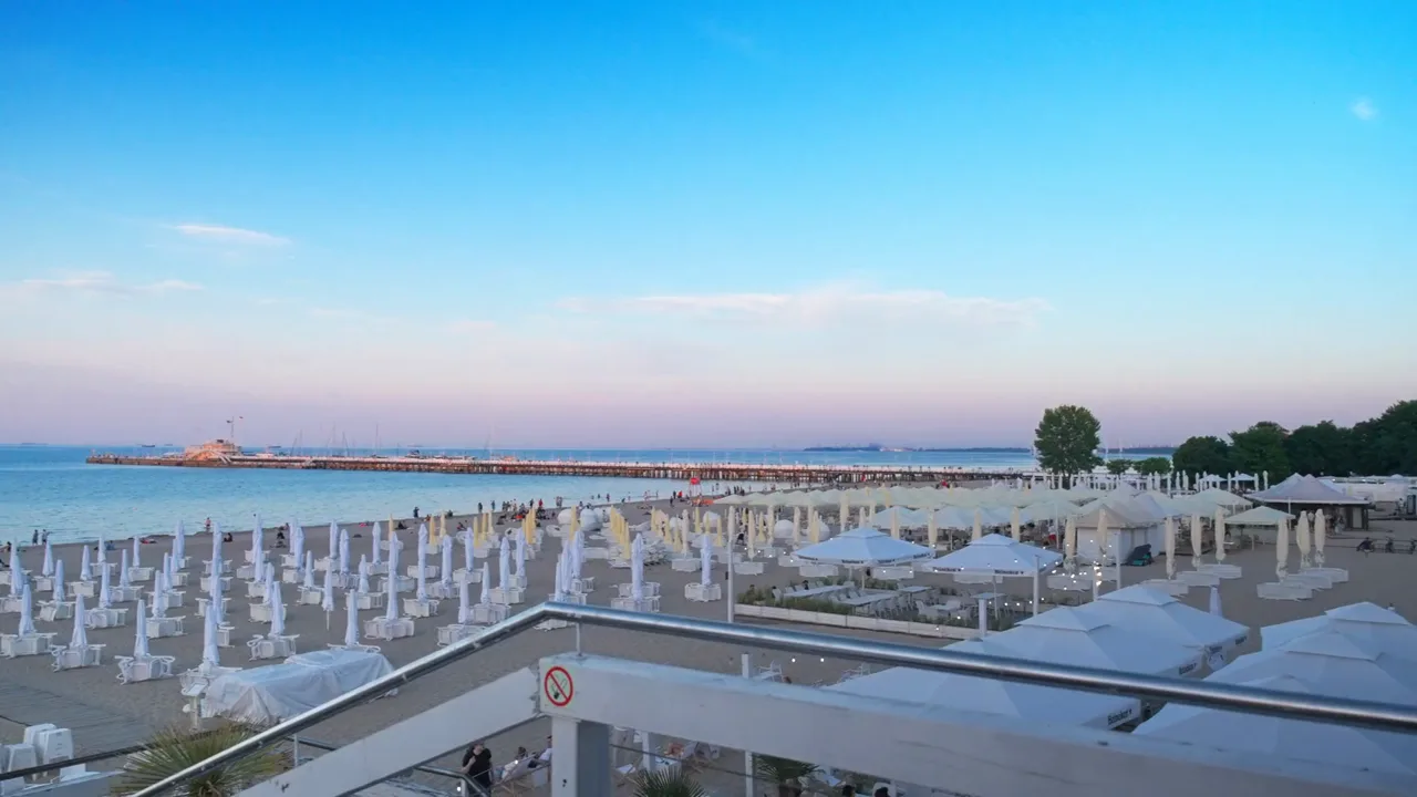 Kadr z sizzle: plaża z parasolami i molo o zmierzchu