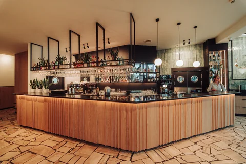 Kontuar barowy z wiszącymi kieliszkami i barmanką pracującą przy alkoholach