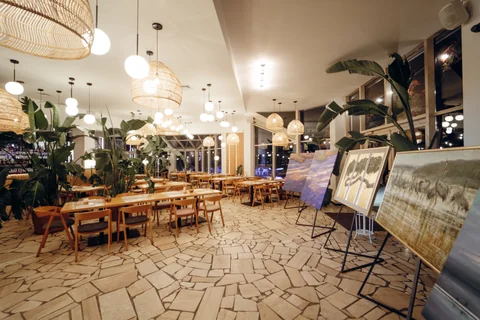 Sala restauracyjna z ratanowymi lampami, roślinami i drewnianymi stołami wieczorową porą