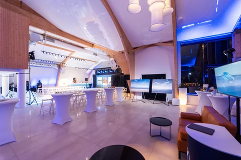 Strefa lounge MUDO ze stolikami, kanapą i ekranem w wieczornym oświetleniu