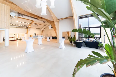 Sala bankietowa z wysokimi stolikami koktajlowymi i widokiem na zieleń za oknem