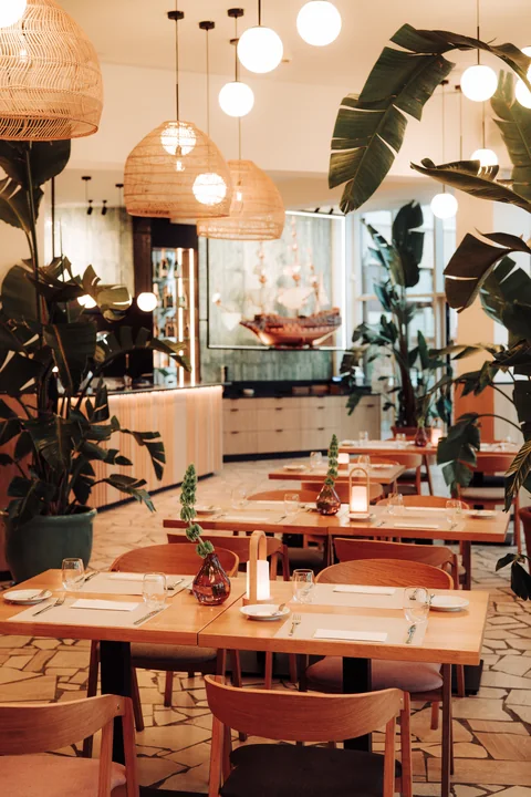 Sala restauracyjna ze stolikami, roślinami i barem w głębi kadru