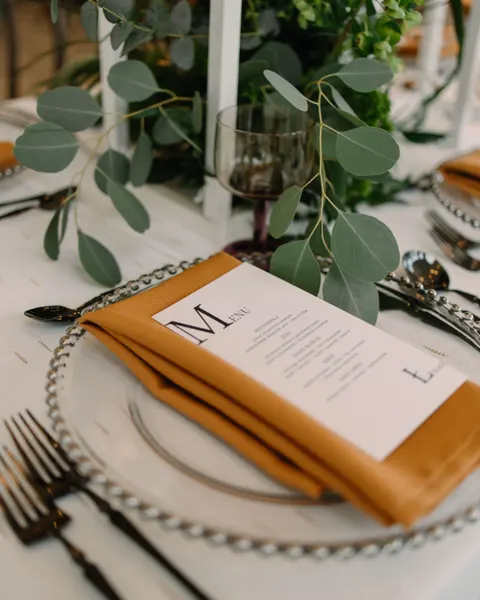 Nakrycie weselne z kartą menu na musztardowej serwetce i gałązką eukaliptusa