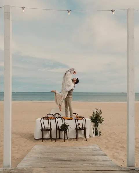 Para młoda pod łukiem na plaży MUDO, przed nią stół i krzesła, w tle morze