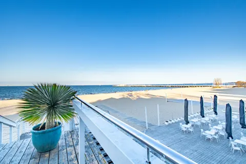 Drewniany taras MUDO z palmą w niebieskiej donicy nad pustą plażą poza sezonem