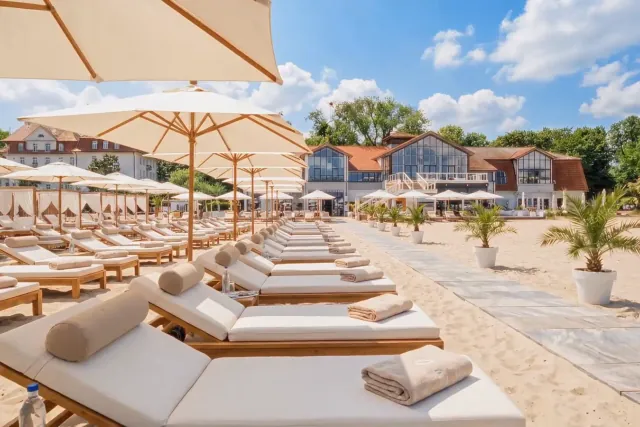 Leżaki z materacami pod parasolami na plaży MUDO, w tle budynki przy plaży