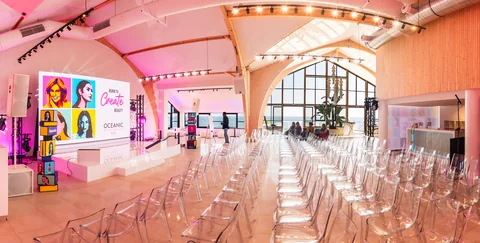 Panorama sali eventowej z ekranem, rzędami krzeseł, barem i widokiem na morze