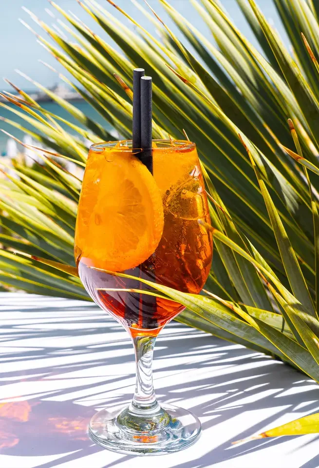 Aperol spritz z plastrem pomarańczy na stoliku w cieniu palmy