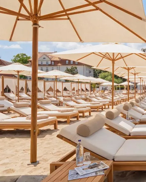 Rzędy leżaków z materacami i wałkami pod parasolami na plaży MUDO, w tle Grand Hotel
