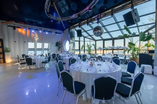 Sala klubowa z przeszklonym dachem: okrągłe stoły z białym nakryciem, kule dyskotekowe i widok na plażę