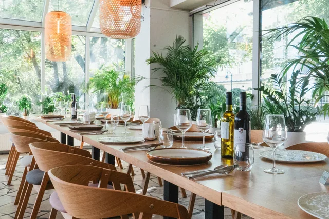 Sala restauracyjna MUDO: nakryte stoły, rattanowe lampy i rośliny pod przeszklonym dachem