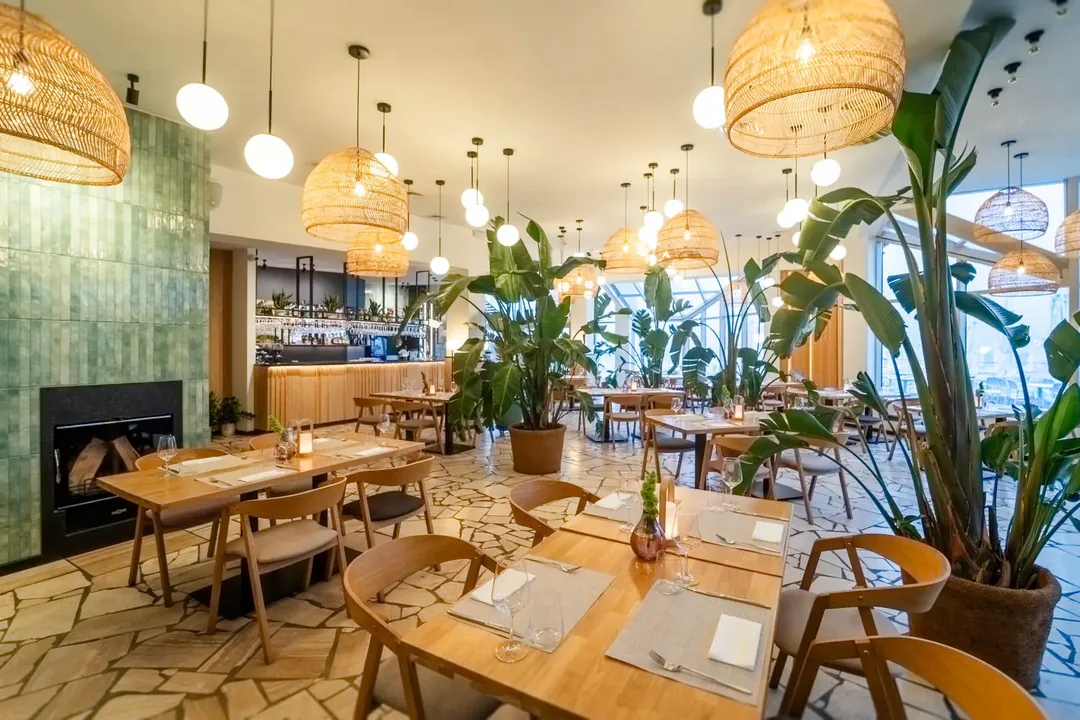 Sala restauracji MUDO za dnia: stoły, lampy z rattanu i zielony kominek